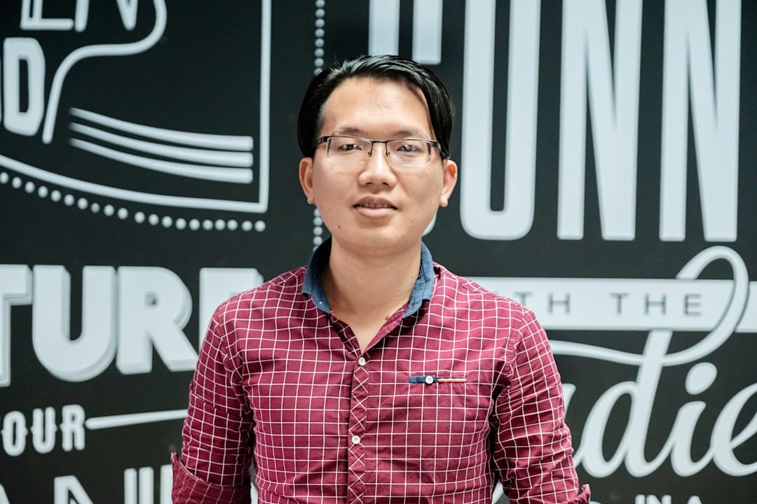 a man wearing glasses standing in front of a sign